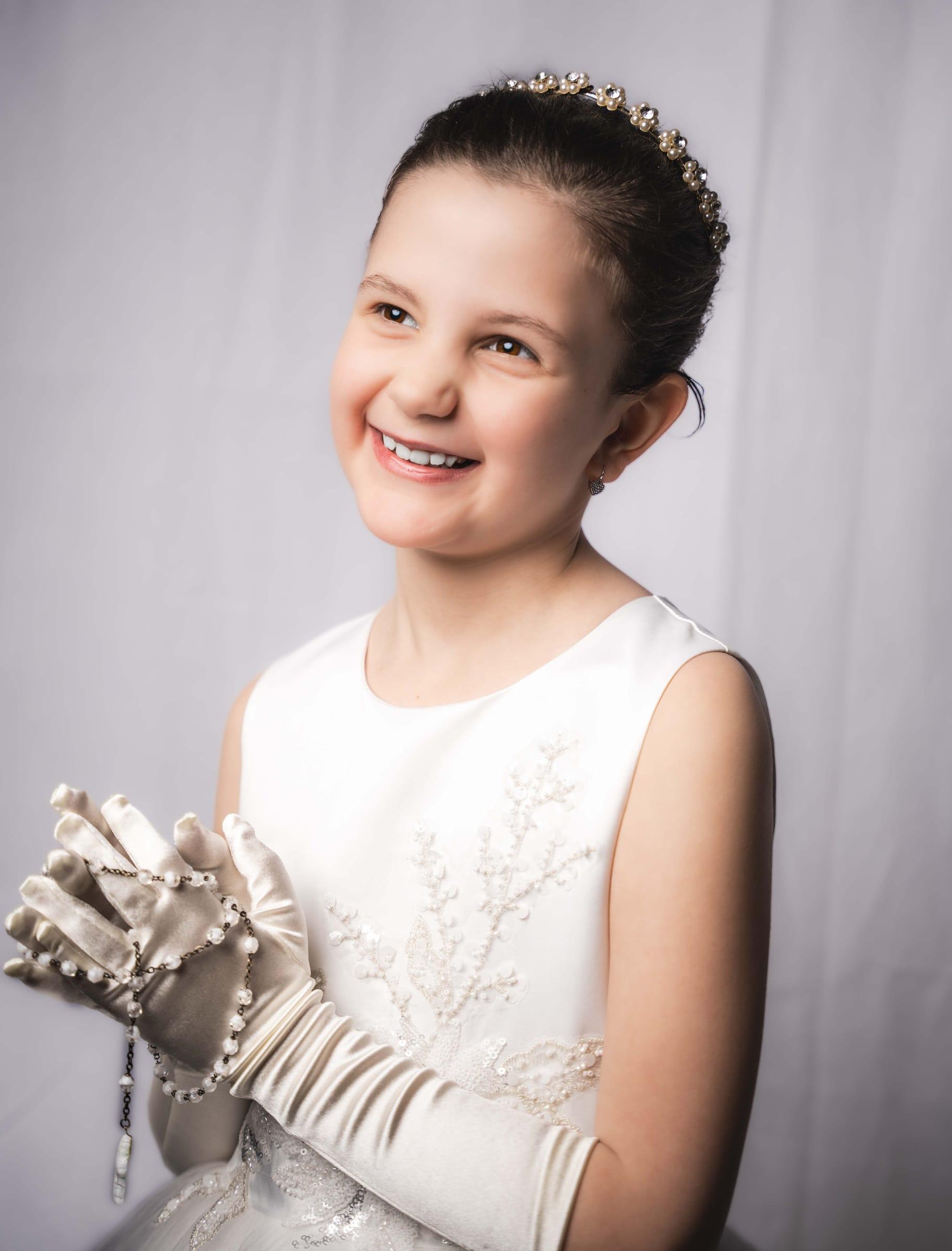 Young girl in a white communion dress smiles in a studio portrait