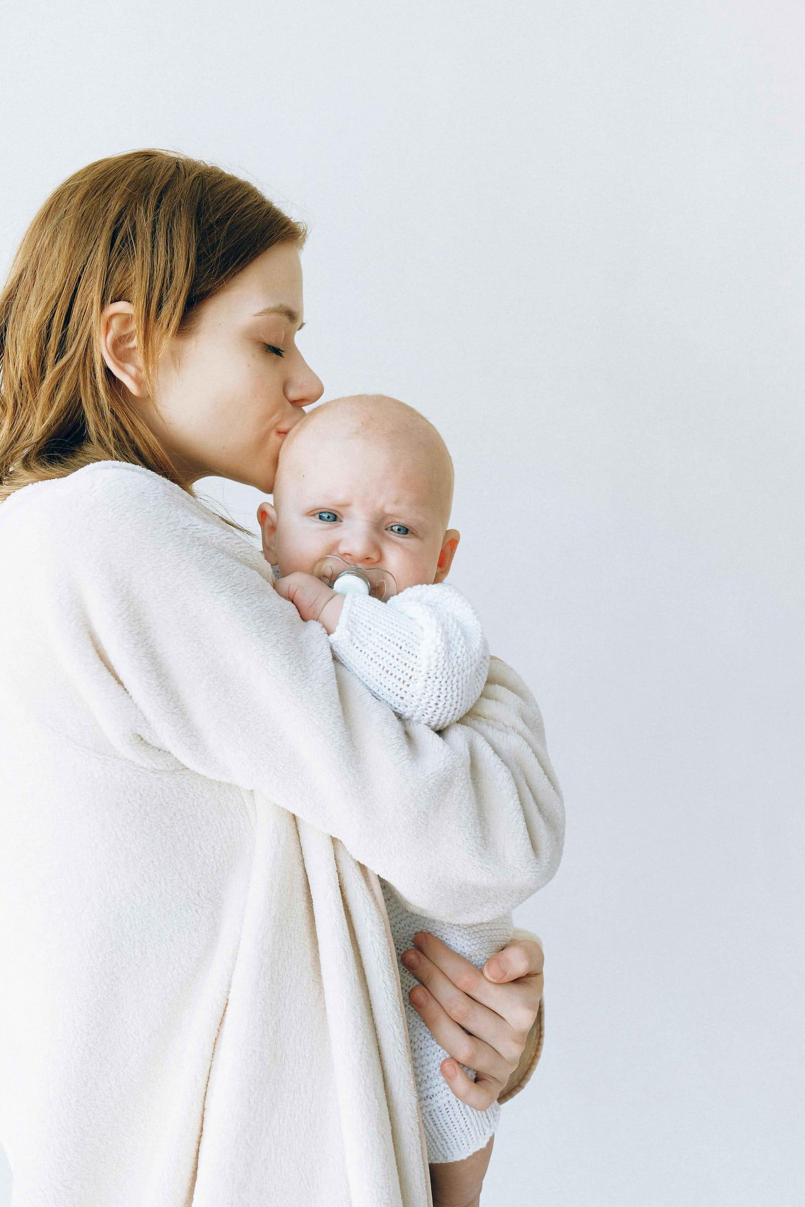 Mother kisses her baby in a bright white studio