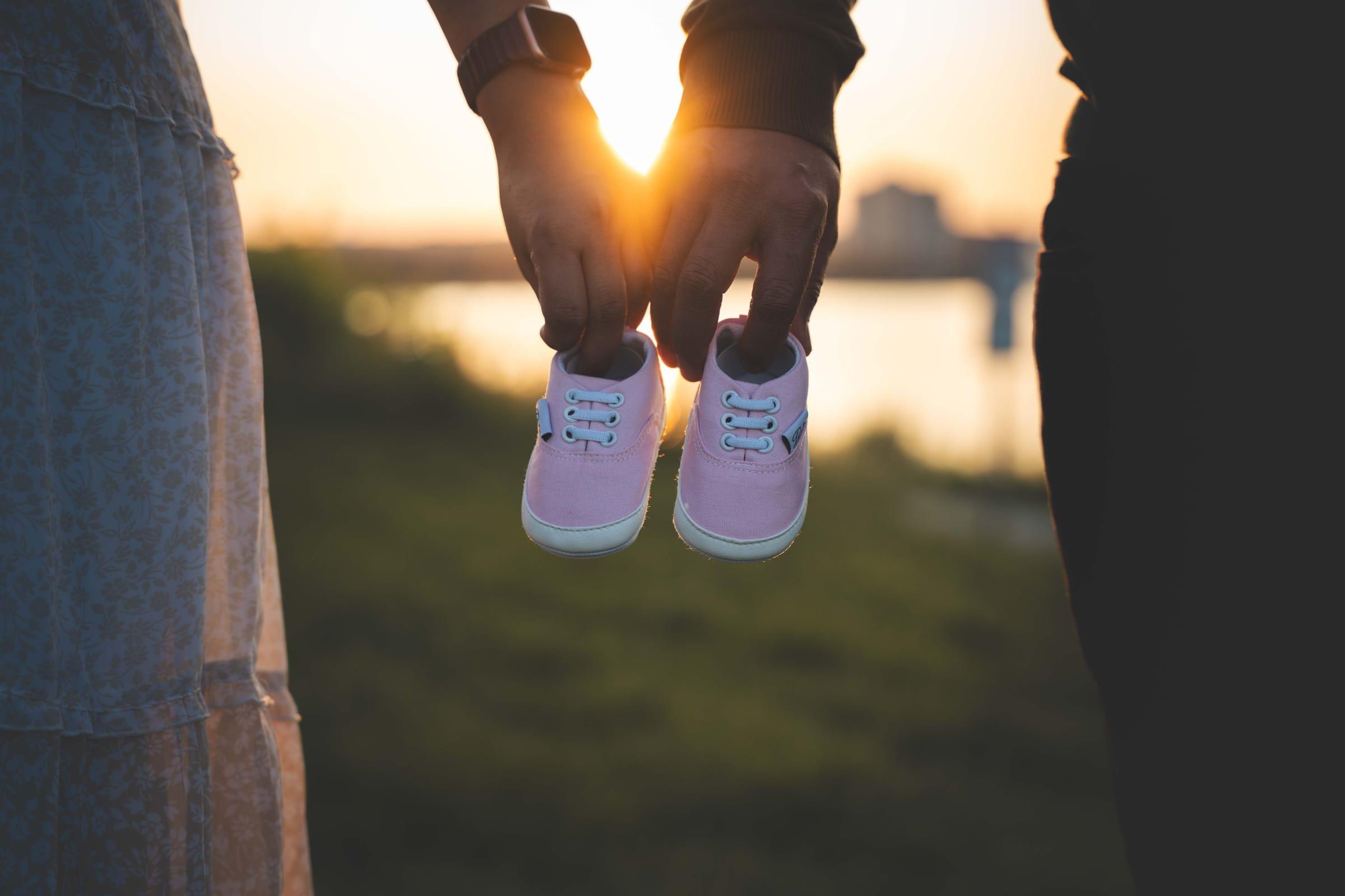 Parents hold tiny baby shoes against the sunset