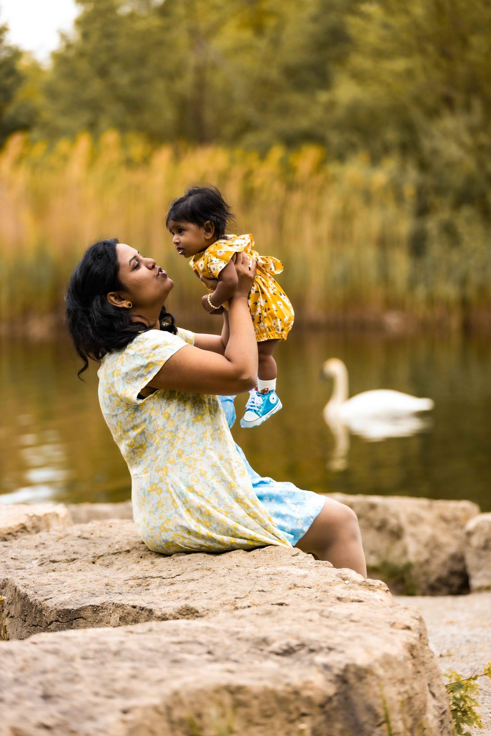 Mother lifts her baby by a lake with a swan, outdoor family session