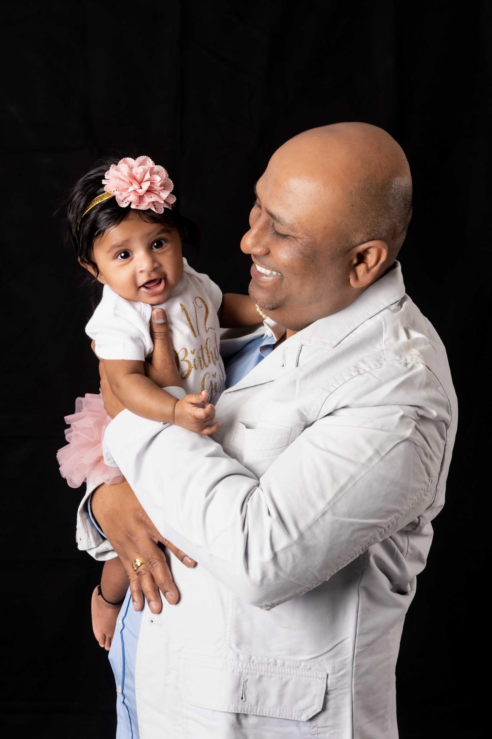 Father holding his baby girl with a flower headband, studio portrait