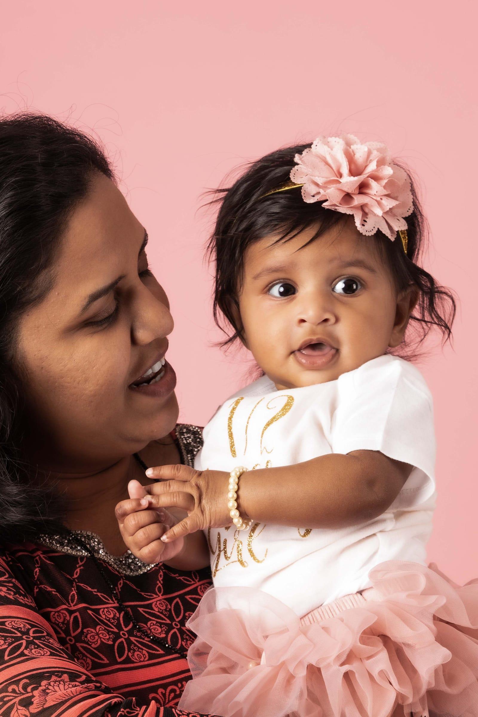 Mother and smiling baby girl on a soft pink backdrop