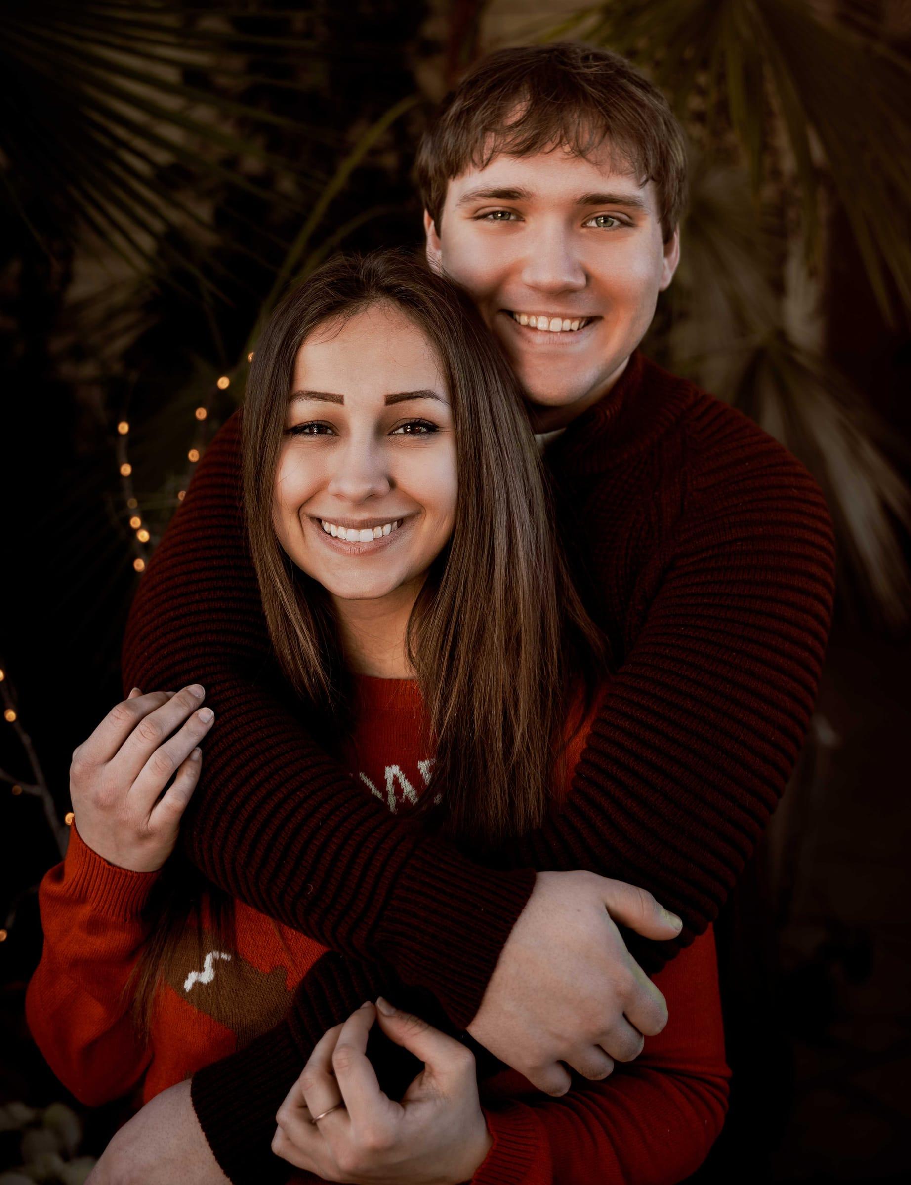 Engaged couple hugging under twinkle lights on a winter evening