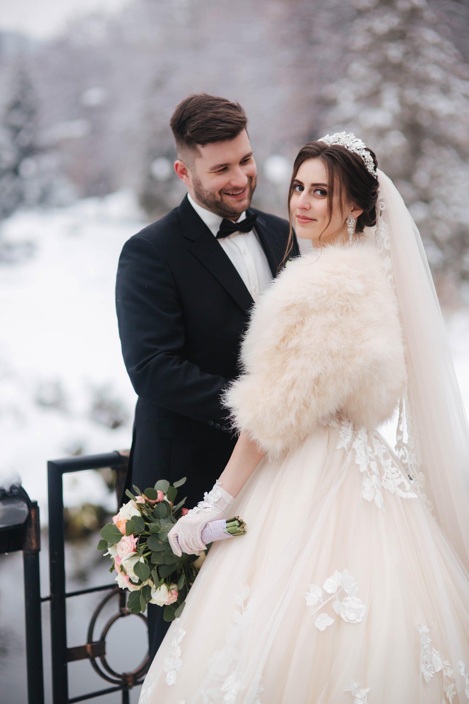 Bride in faux-fur stole and groom in tuxedo pose in the snow, Toronto winter wedding
